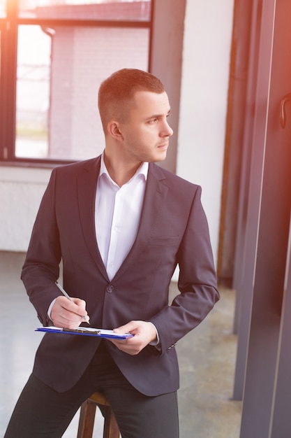 Apuesto hombre de negocios vistiendo un traje negro con un portapapeles