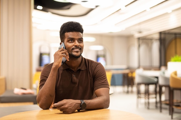 Apuesto hombre negro en la cafetería a través de teléfono móvil