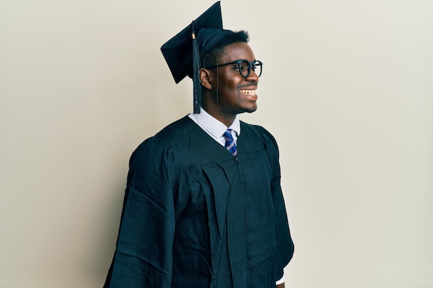 Apuesto hombre negro con gorra de graduación y túnica de ceremonia mirando de lado a lado con una sonrisa en la cara expresión natural riendo confiado