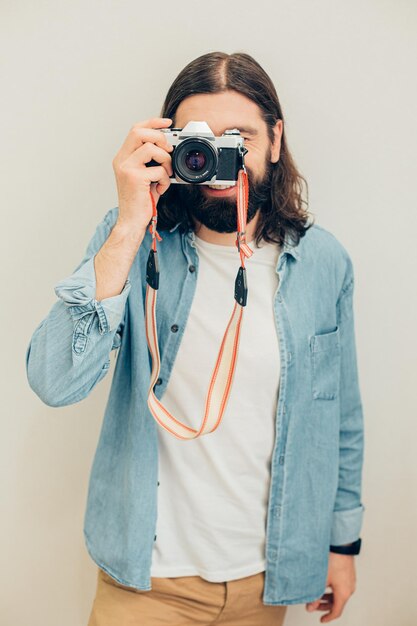 Un apuesto hombre de pelo largo sonriendo y sintiéndose feliz mientras toma fotos con su cámara