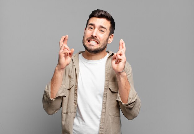 Apuesto hombre rubio adulto cruzando los dedos con ansiedad y esperando buena suerte con una mirada preocupada