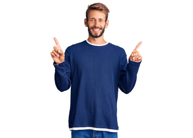 Un apuesto hombre rubio con barba que usa suéter casual sonriendo confiado señalando con los dedos en diferentes direcciones. copiar espacio para publicidad