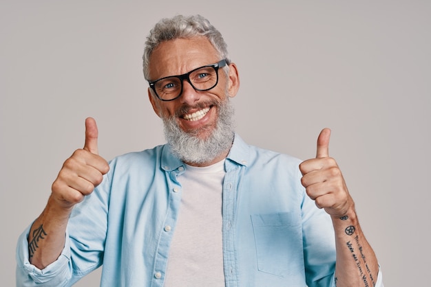 Apuesto hombre senior en anteojos manteniendo los pulgares hacia arriba y sonriendo