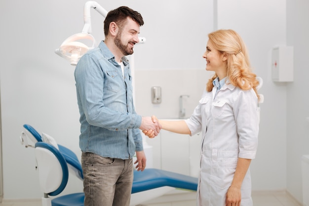 Apuesto hombre sonriente agradecido expresando su gratitud y dando la mano a los médicos después de que le trataran los dientes