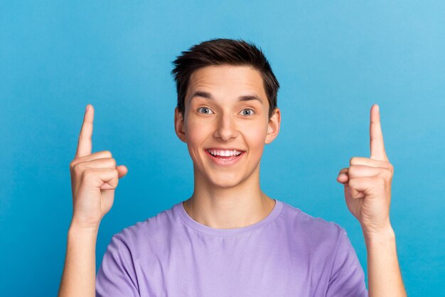 Apuesto hombre sonriente apuntando hacia arriba oferta de espacio vacío aislado sobre fondo de color azul