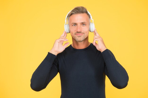 Un apuesto hombre sonriente escucha música con elegantes auriculares con calidad de sonido de fondo amarillo