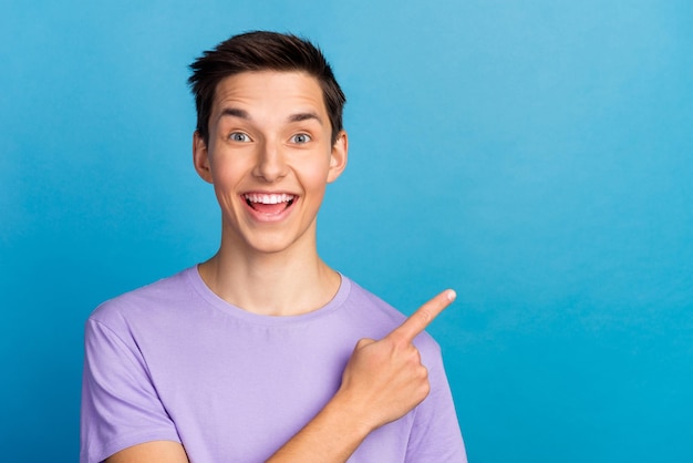 Apuesto hombre sonriente señalando el espacio vacío anuncios increíbles aislado sobre fondo azul.