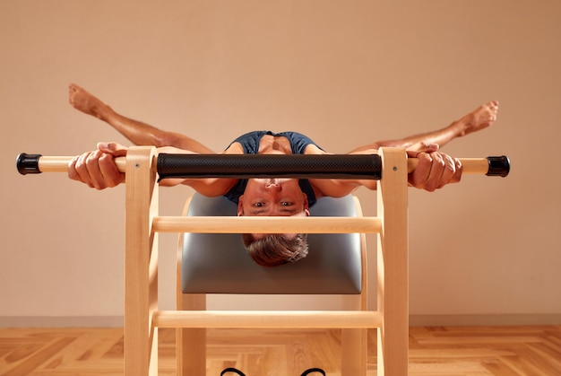 Apuesto instructor masculino de pilates realizando ejercicio de fitness de equilibrio de estiramiento en equipos de barril pequeño en el estudio de pilates interior moderno interior