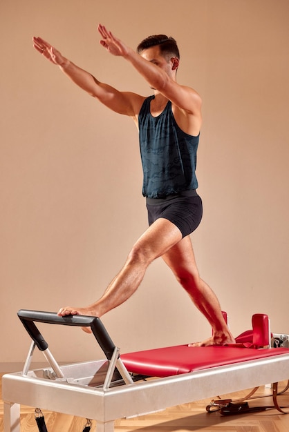 Apuesto instructor masculino de pilates realizando ejercicio de fitness de equilibrio de estiramiento en equipos de barril pequeño en el estudio de pilates interior moderno interior