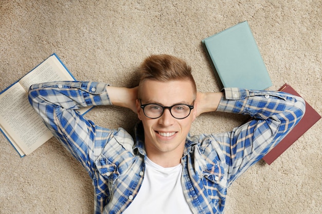 Apuesto joven acostado en la alfombra con libros