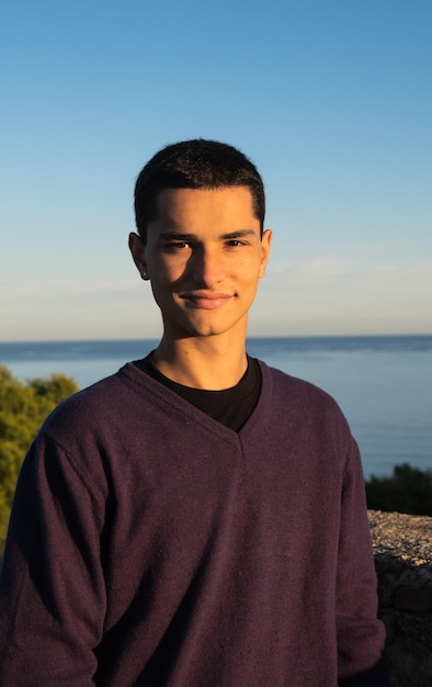 Apuesto joven con actitud positiva posando para la cámara con el mar de fondo