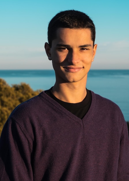 Apuesto joven con actitud positiva posando para la cámara con el mar de fondo