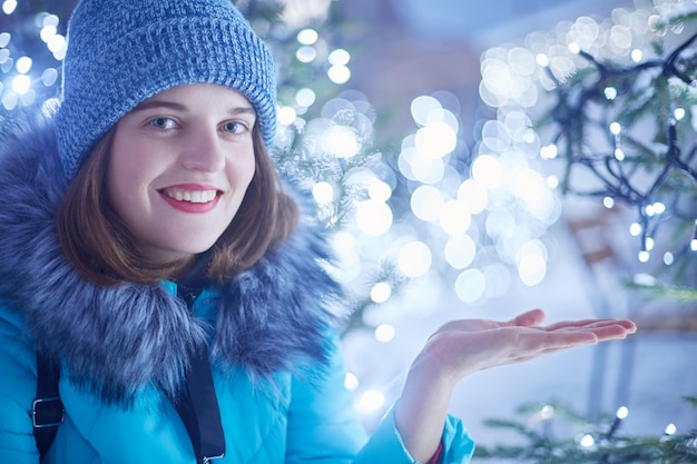 Apuesto joven adorable mujer atrapa copos de nieve, se viste con ropa abrigada de invierno, se encuentra al aire libre, disfruta del invierno