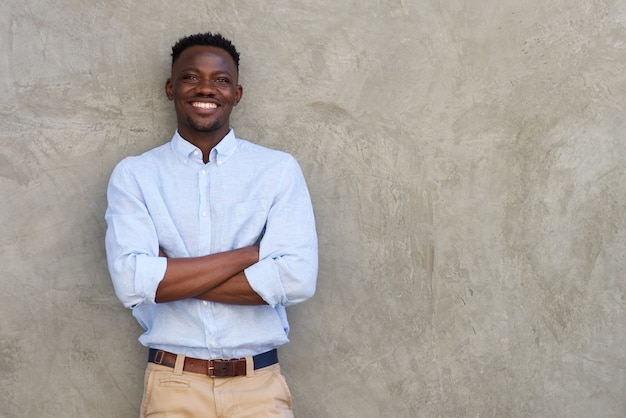 Apuesto joven africano sonriendo con los brazos cruzados por la pared