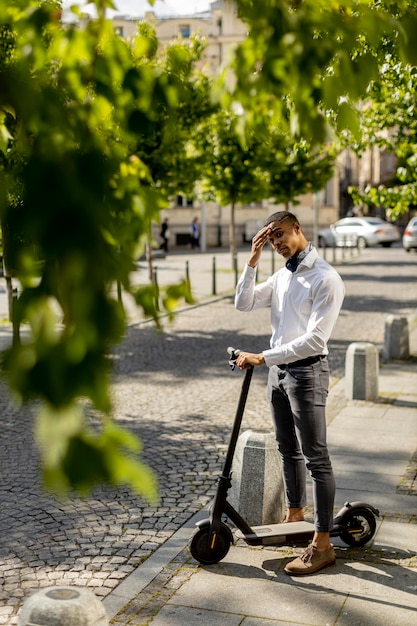 Apuesto joven afroamericano usando scooter eléctrico y esperando para cruzar la calle