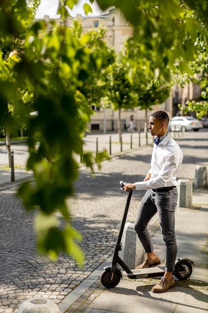 Apuesto joven afroamericano usando scooter eléctrico y esperando para cruzar la calle