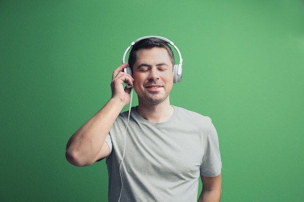 Apuesto joven en auriculares escuchando música sobre fondo de color