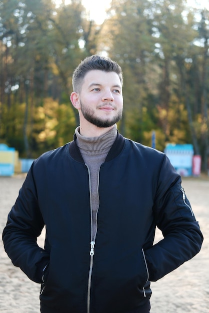 Apuesto joven con barba y chaqueta negra posando en la playa Vida lenta Disfrutando de las pequeñas cosas Concepto Lykke