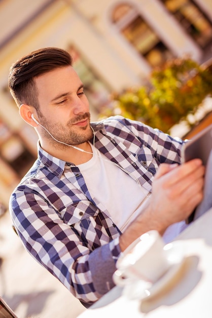 Apuesto joven bebiendo café y escuchando música en un teléfono inteligente.