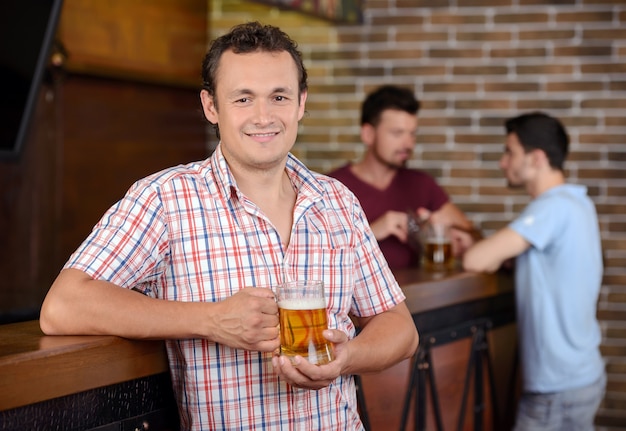 Apuesto joven bebiendo cerveza en el bar y sonriendo.