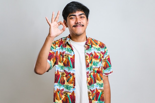 Apuesto joven con bigote vistiendo camiseta casual sobre fondo blanco sonriendo positivo haciendo bien firmar con la mano y los dedos. expresión exitosa.