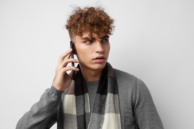 Apuesto joven en una bufanda a cuadros mirando el fondo claro de la moda del teléfono