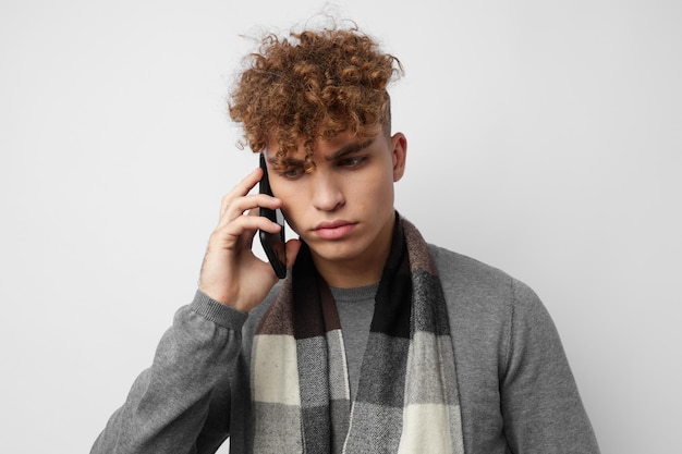 Apuesto joven en una bufanda a cuadros mirando el fondo claro de la moda del teléfono