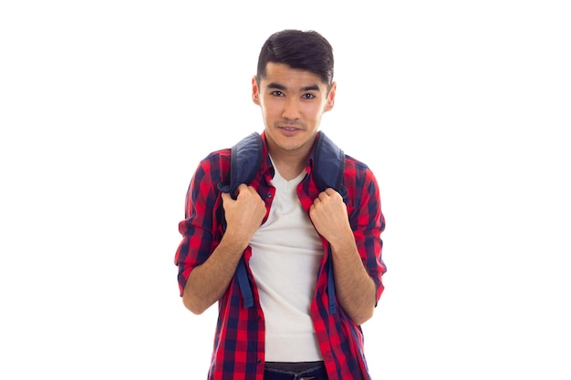 Apuesto joven con cabello negro en jeans camiseta blanca y camisa a cuadros con mochila azul