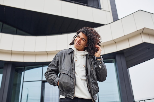 Apuesto joven con cabello negro rizado posando para la cámara en la calle contra el edificio.