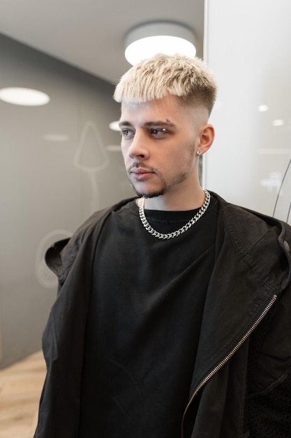 Apuesto joven con cabello en ropa negra de moda con camiseta negra y capucha negra en el interior