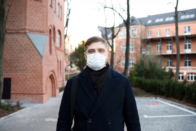 Apuesto joven caminando con mascarilla en una zona residencial durante la pandemia y cuarentena global de covid-19 coronavirus