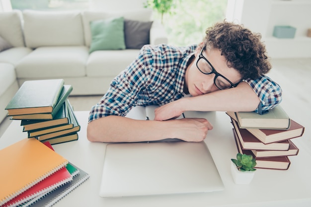 Apuesto joven cansado en casa nerd con gafas durmiendo cara en libros