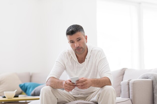 Apuesto joven casual usando un teléfono móvil en casa de lujo