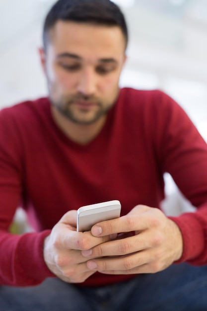 Foto apuesto joven casual usando un teléfono móvil en casa