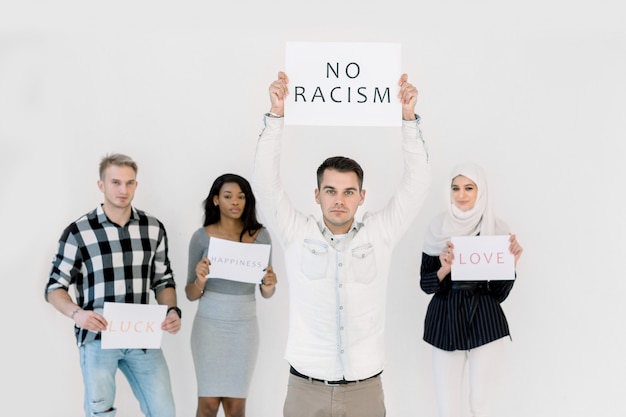 Apuesto joven caucásico protesta con un cartel, No hay concepto de racismo, junto con tres amigos multiétnicos