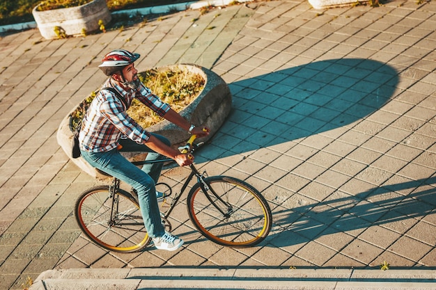 Un apuesto joven va a la ciudad con su bicicleta. Él está montando en bicicleta, feliz por el buen tiempo.