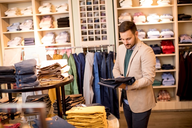 Apuesto joven comprando pantalones en tienda de moda