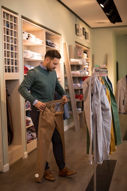 Apuesto joven comprando pantalones en tienda de moda