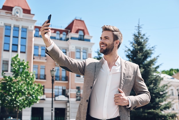 Apuesto joven elegante tomando un selfie en la ciudad