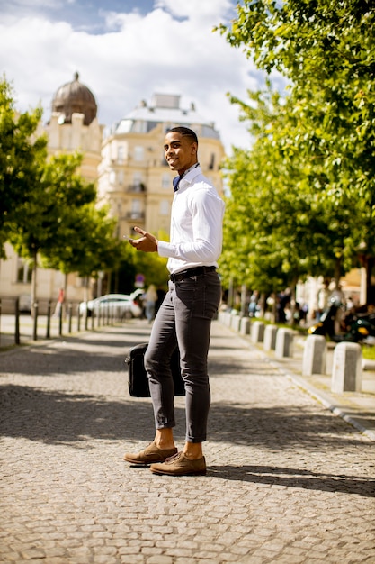 Apuesto joven empresario afroamericano mediante un teléfono móvil en una calle