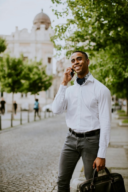 Apuesto joven empresario afroamericano mediante un teléfono móvil mientras espera un taxi esperando un taxi en una calle