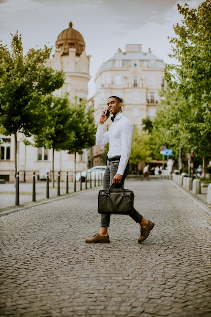 Apuesto joven empresario afroamericano usando un teléfono móvil mientras ceossing una calle