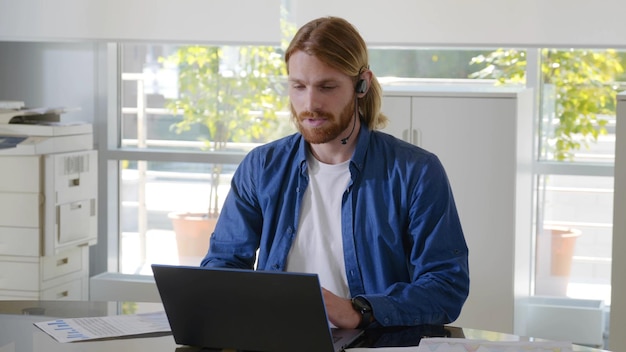 Apuesto joven empresario en auriculares viendo webinar en la computadora portátil en la oficina moderna