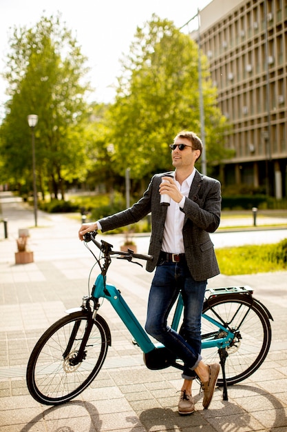 Apuesto joven empresario en la bicicleta eléctrica con taza de café para llevar