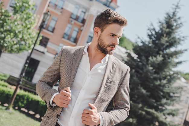 Apuesto joven empresario caminando por las calles de la ciudad en la mañana para ir a trabajar en la oficina llevar ropa casual elegante de chaqueta marrón y camisa blanca. Estilo de vida urbano de los jóvenes profesionales.