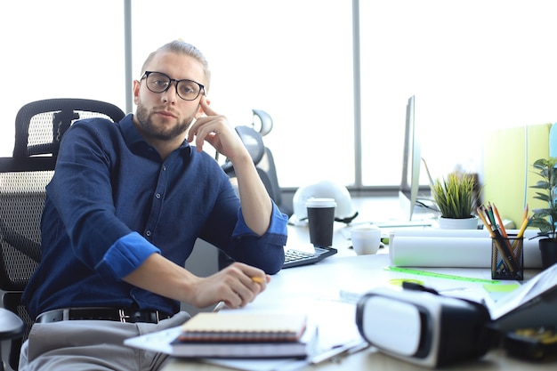 Apuesto joven empresario mirando a cámara mientras está sentado en la oficina.