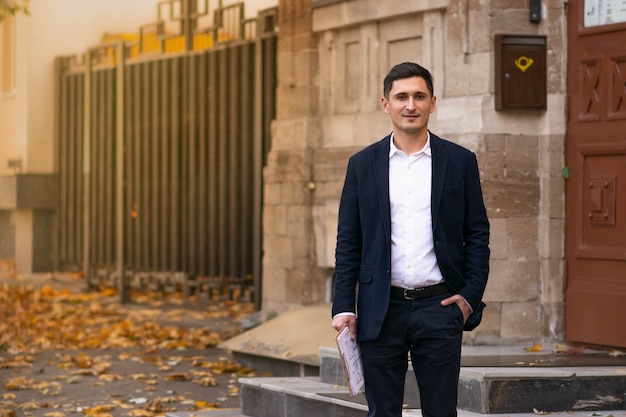 Apuesto joven empresario de pie afuera y sonriendo con confianza. Retrato de negocios.