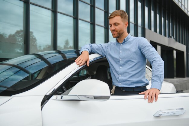 Apuesto joven empresario de pie cerca de su coche al aire libre