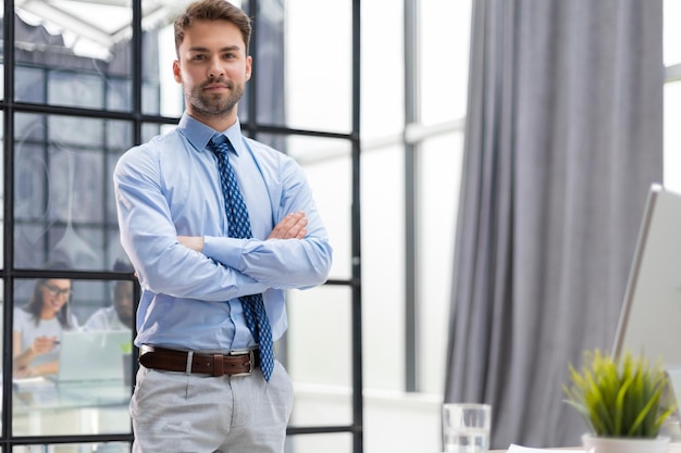 Apuesto joven empresario de pie en la oficina moderna con colegas en el fondo