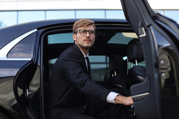 Apuesto joven empresario serio sentado en su cómodo coche nuevo e ir a la oficina.